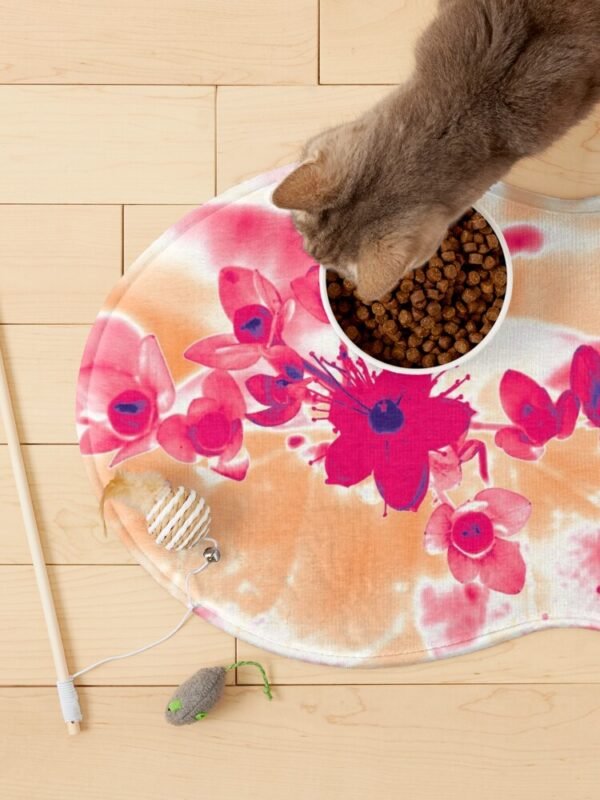 A cat eating from a bowl of food which is sitting on an Alternative Hypericum fish shaped mat. There are cat toys lying around.