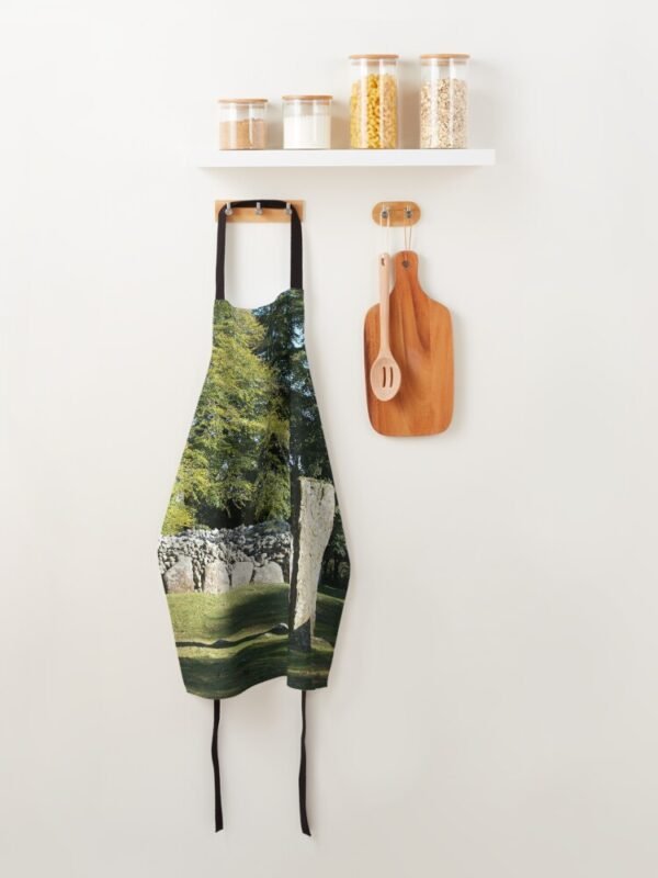 Cairns and Standing Stone Apron hanging on some wooden pegs below a shelf and next to a hanging board and spoon