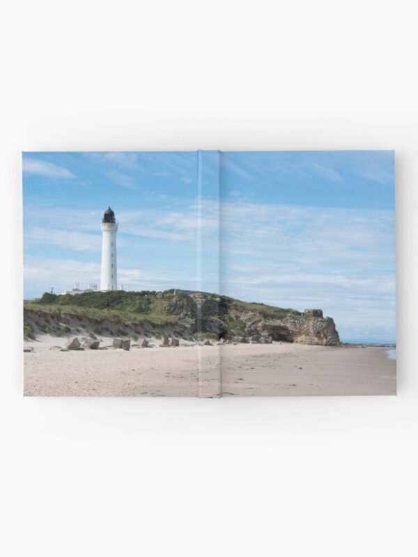 A hardcover journal with an image of a lighthouse on rocks on a sandy beach