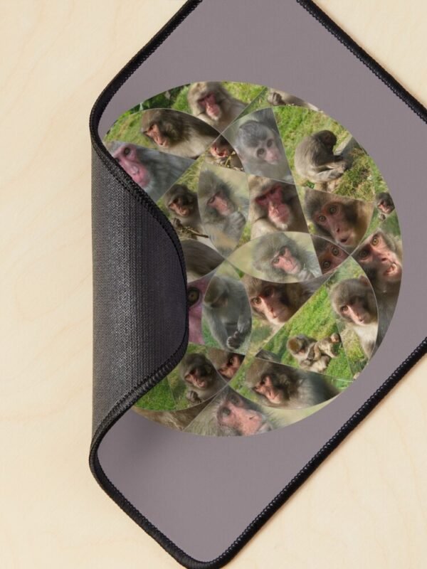 A mouse mat/pad with the Many Faces of A Snow Monkey design. One of the corners is curled to show the backing.