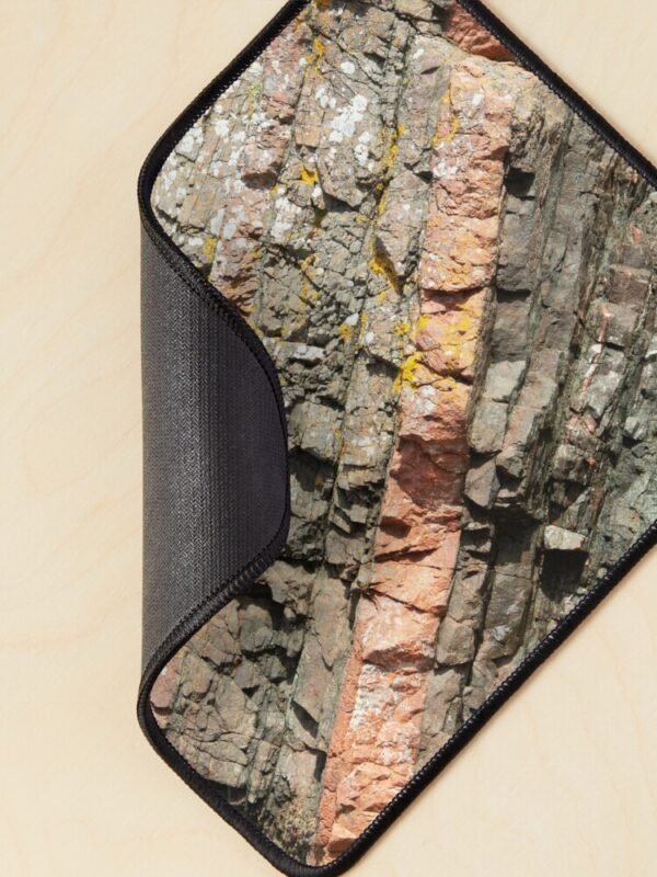 A mouse mat/pad with a close up image of different coloured layers of rock on its front. The corner is curled to display the backing.